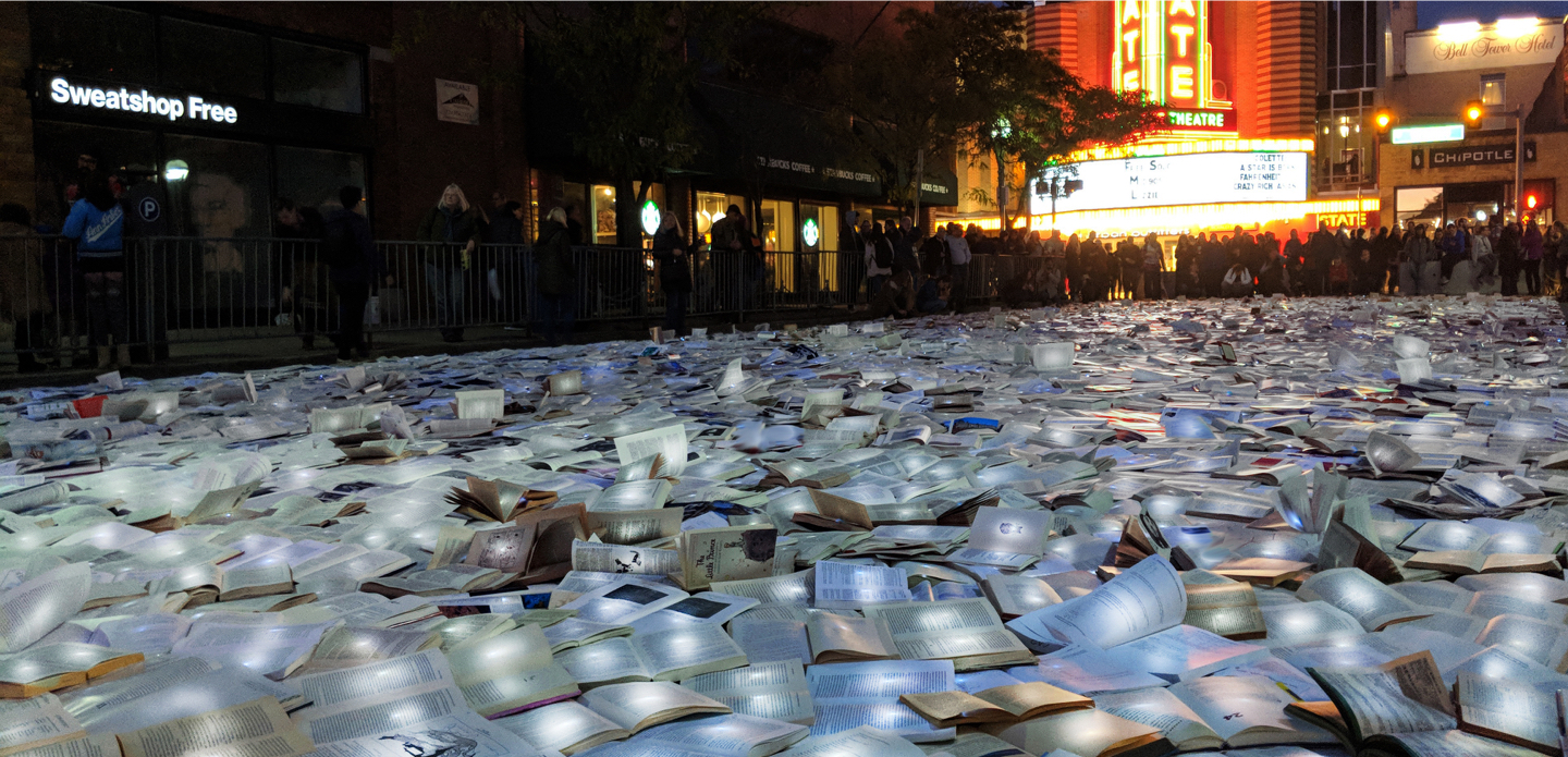 With the State Theatre in the background, a crowd of people look at illuminated books laid out on the street.