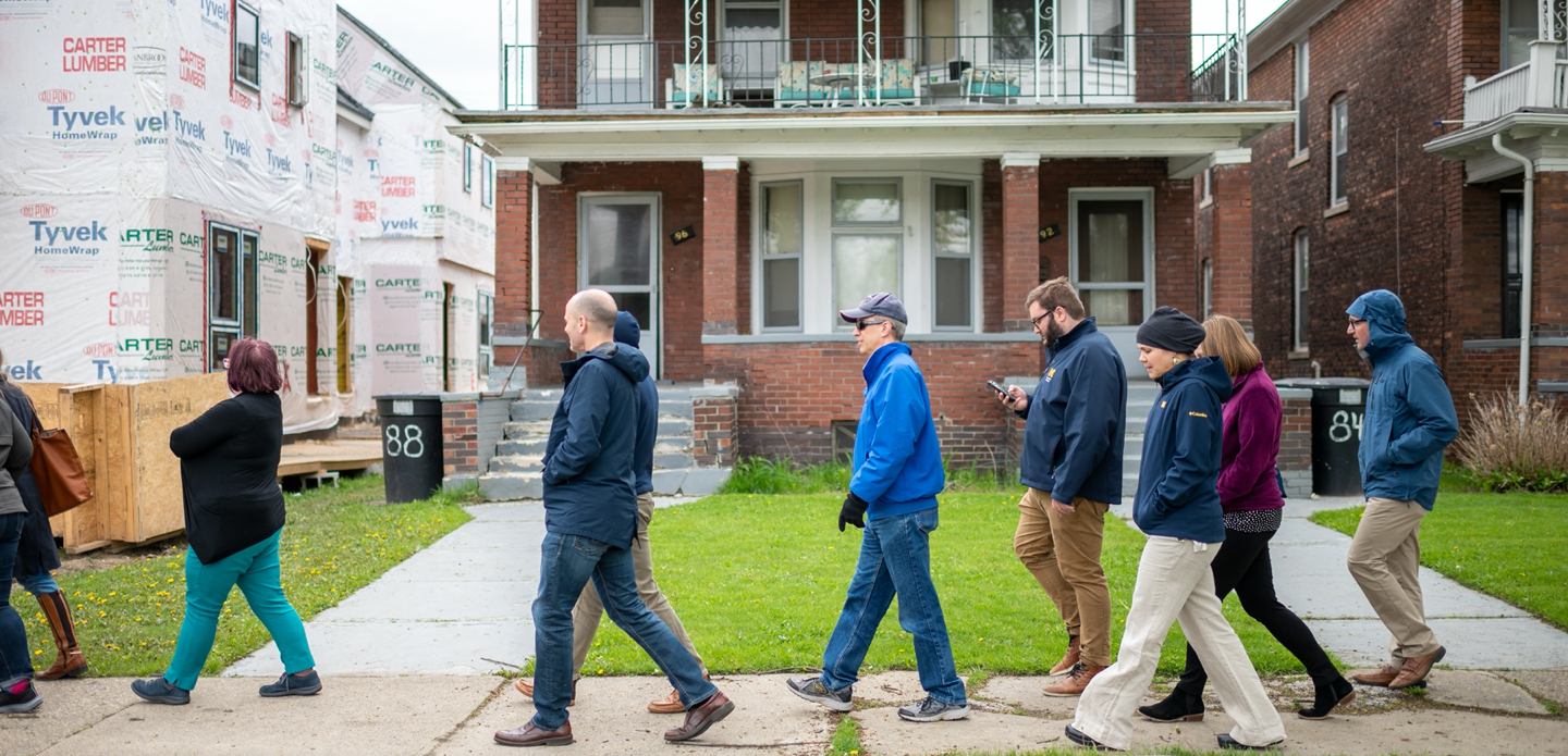 U-M faculty and staff walk past red-brick houses in Detroit.