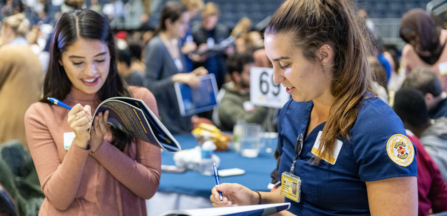 Two female U-M students take notes at the IPE event.