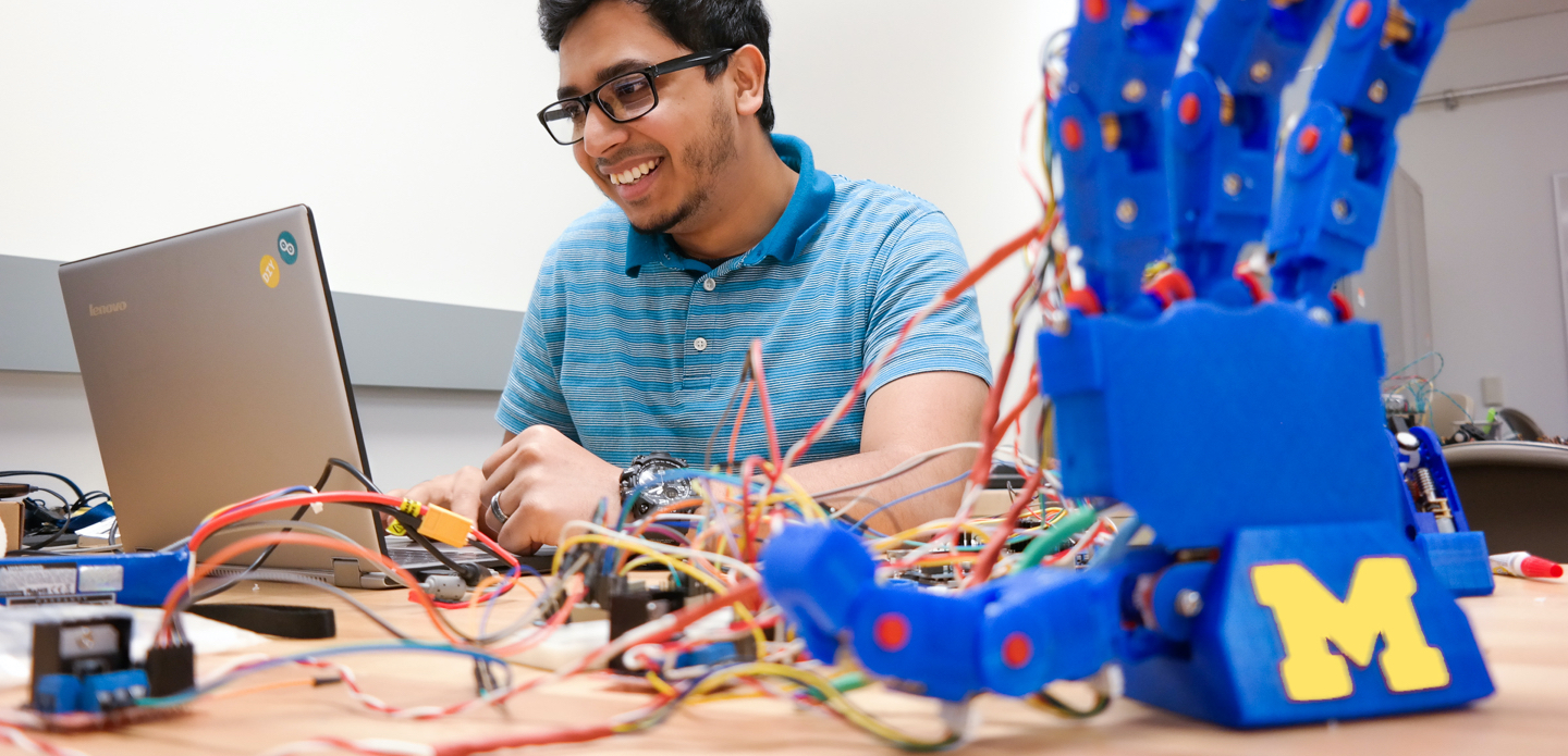 Male UM-Dearborn mechanical engineering student works on a humanoid robotic hand.