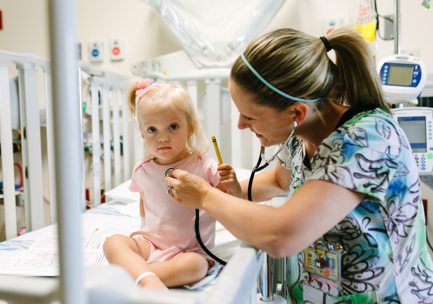 A U-M nurse uses a stethoscope on a toddler in a hospital room.