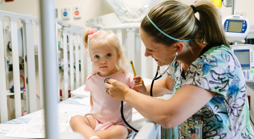 A U-M nurse uses a stethoscope on a toddler in a hospital room.